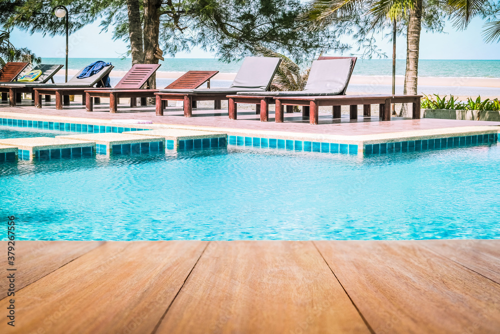 Image of wood table in front of a swimming pool background. Brown wooden desk empty counter in front of the poolside on beautiful beach resort and outdoor spa vacation day.