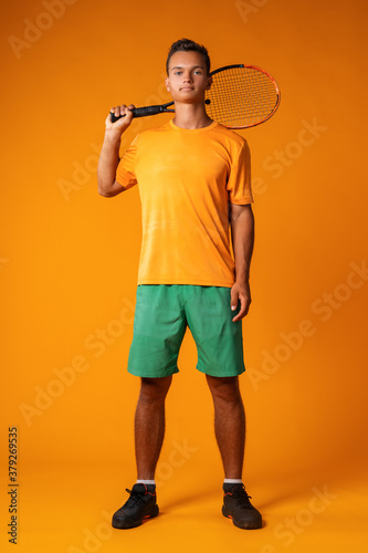 Full-length portrait of a tennis player man in action against orange background © fotofabrika