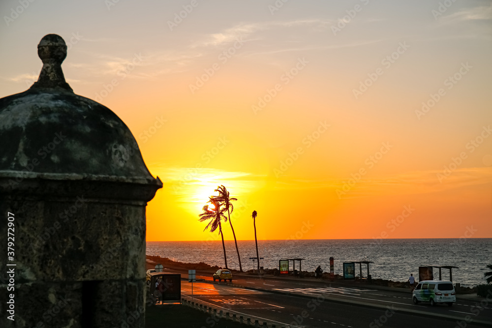 Beautiful sunset sky over the sea with palm trees and building in front from the city wall, Cartagena, Colombia