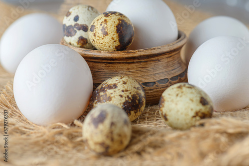 White raw chicken eggs and small quail eggs in a clay bowl on a burlap close-up. Chicken and quail eggs rustic background.