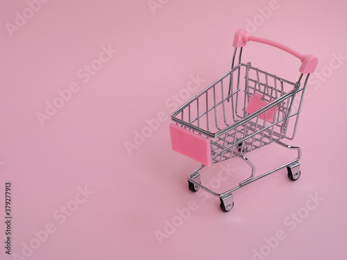 Small shopping cart with big cucumber on pink background