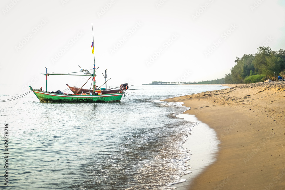 Fototapeta premium Beautiful view of the turquoise waves with the blue sky and white clouds and fisherman's boat on sandy beach on vacation in Hua Hin, Prachuap Khiri Khan Province, Thailand.