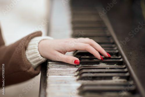 Close-up of a manicured hand playing the piano. Red varnish
