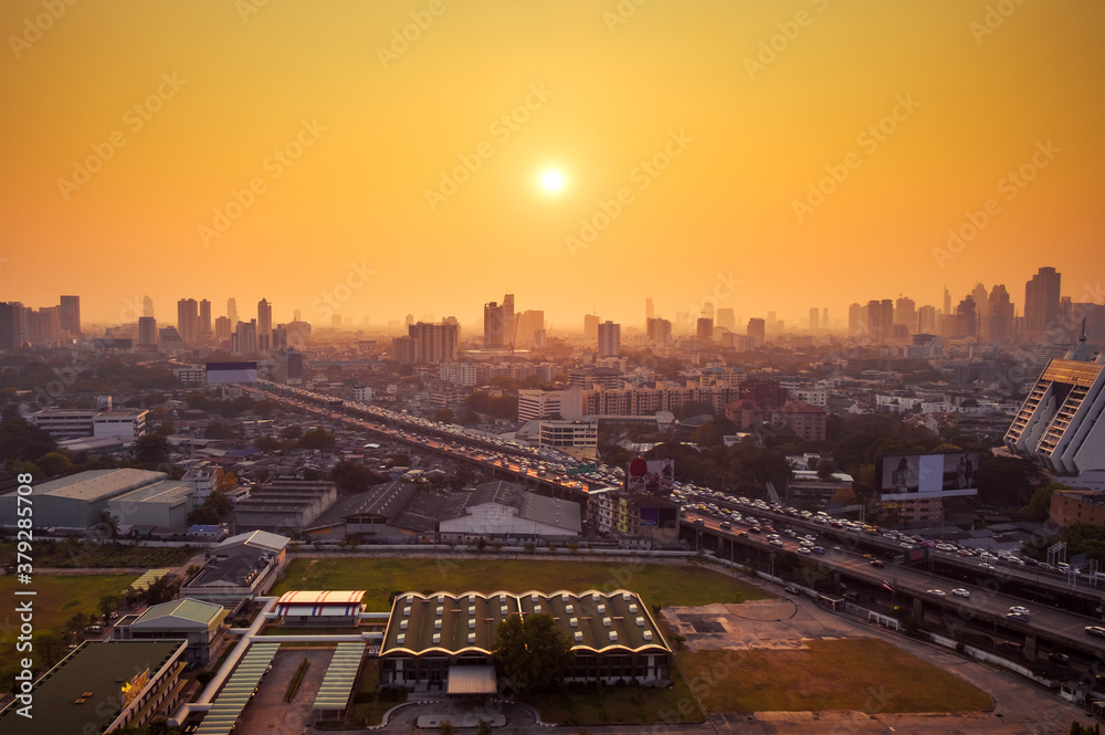 Fototapeta premium Aerial view of the modern buildings finance and highway at sunset of Bangkok City, Thailand. The car in evening on the road going to the town. The speed traffic trails on motorway.