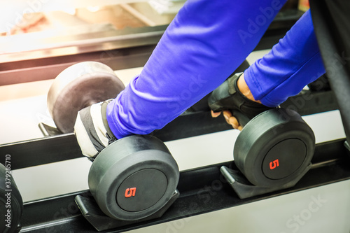 Closeup hand of young man working out lifting weight dumbbells in the gym.
