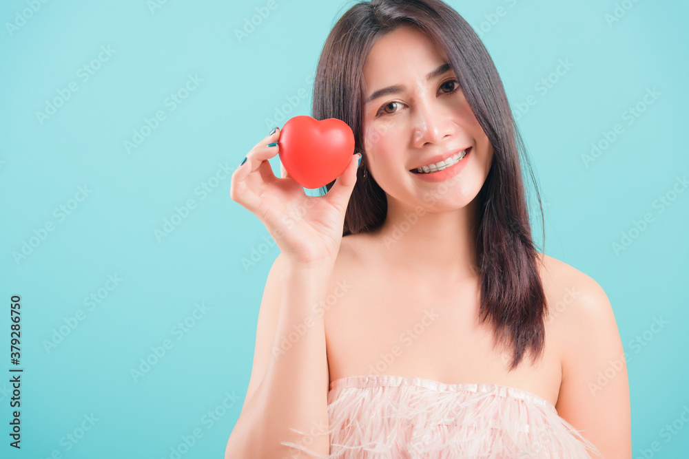 Asian happy portrait beautiful young woman standing smile holding red heart on hand near face on blue background with copy space for text Asian happy portrait beautiful young woman standing smile holding red heart on hand near face on blue background with copy space for text