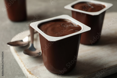 Fotografie Board with plastic cups of yogurt and spoons on gray background