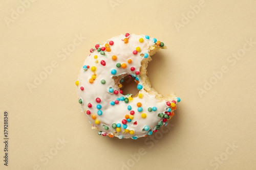 Tasty bitten donut on beige background, top view