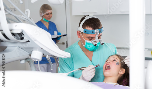 Confident male dentist treating teen girl patient in modern dental office