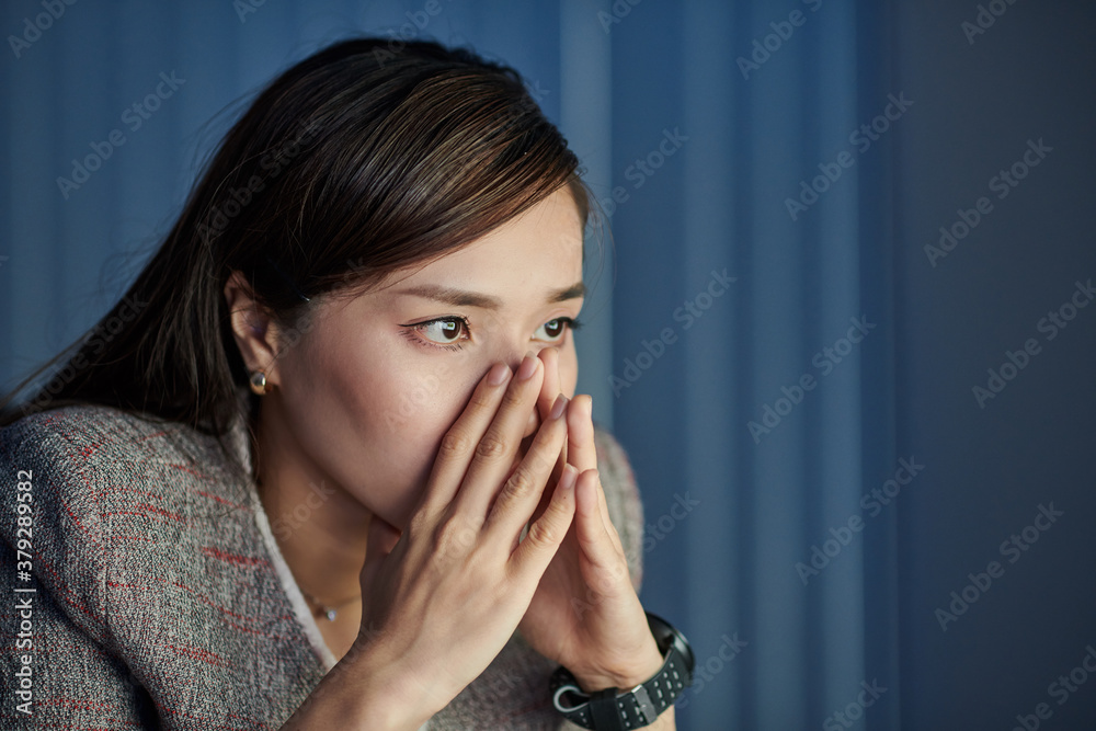 Shocked stressed young Asian businesswoman reading e-mail with bad news on glowing sreen of computer
