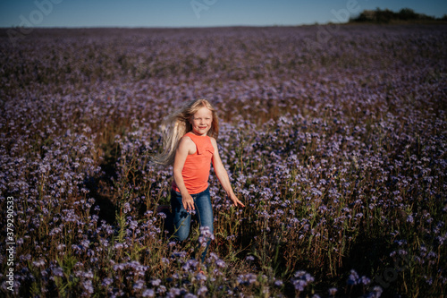 happy child, blond girl runs and jumps in violet flower field. Reconnection with nature.