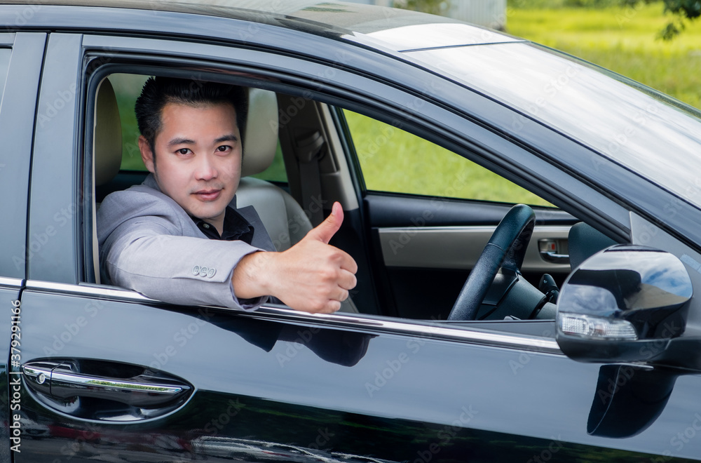 Happy businessman while driving car and smiling on his morning commute to work. Handsome Asian young man his thumbs up on luxury automobile in the road trip.