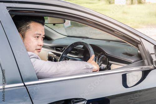 Happy businessman while driving the car and smiling on his morning commute to work. Executive handsome Asian young man on his luxury automobile on the road trip. © Chaiyaphruek