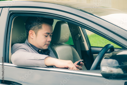Happy businessman using smartphone calling while driving the car on his morning commute to work. Handsome Asian young man touching mobile phone communication on his luxury automobile on the road trip.