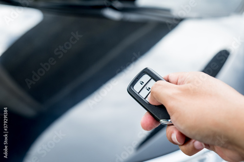 Businessman opens his luxurious car door with a modern remote control key. The young man is locking the automobile with the security system. Keyless in male hand with copy space.
