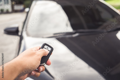 Businessman opens his luxurious car door with a modern remote control key. The young man is locking the automobile with the security system. Keyless in male hand.