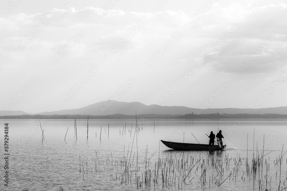 Two men on a little boat fishing in a lake Two men on a little boat fishing in a lake