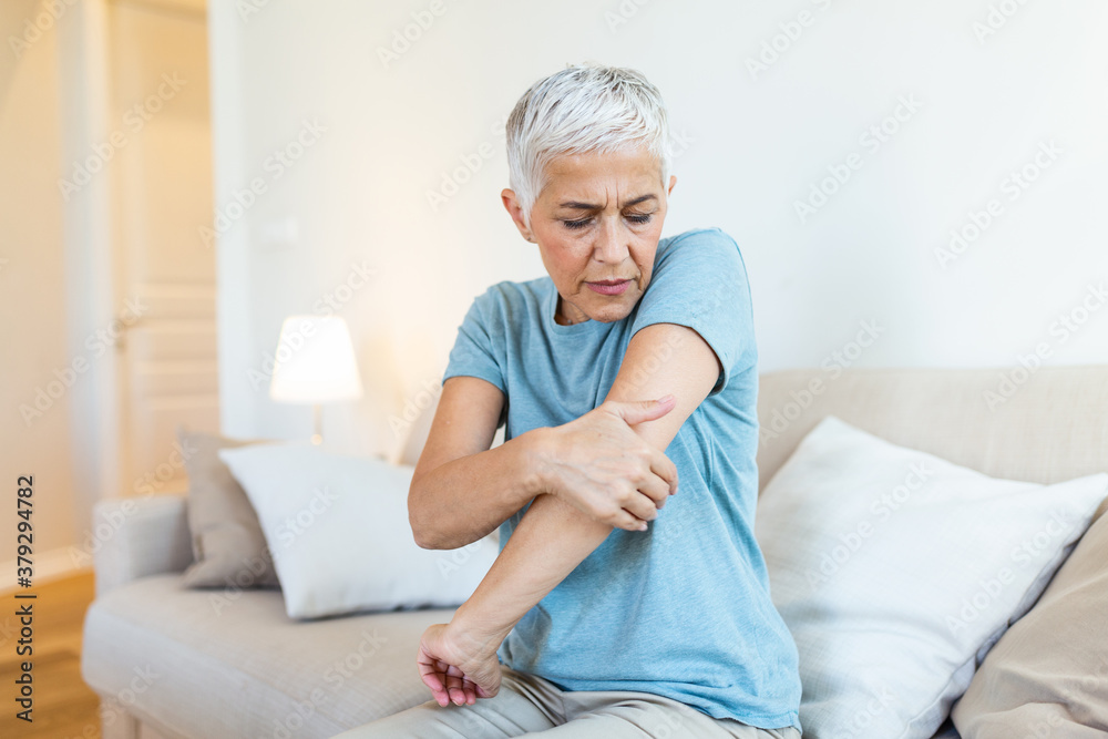 Old age, health problem and people concept - close up of senior woman suffering from pain in hand at home. woman hand holding her elbow suffering from elbow pain. Old age, health problem and people concept - close up of senior woman suffering from pain in hand at home. woman hand holding her elbow suffering from elbow pain.