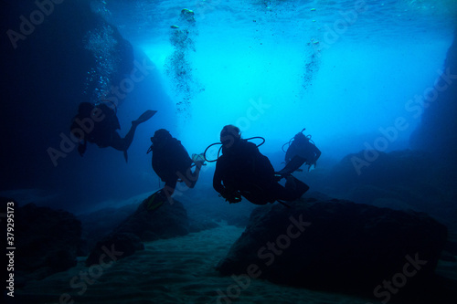 Scuba divers black silhouettes in a blue cave making bubbles