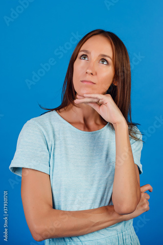 Portrait of a brooding brunette in a blue t-shirt, looking into an empty space, isolated on a blue background.