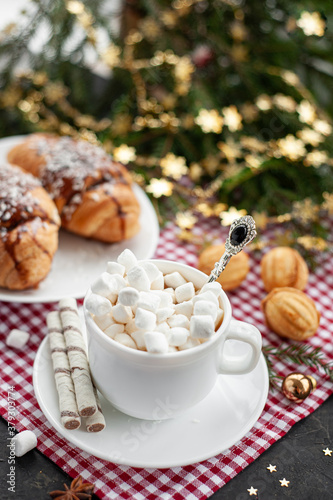 Christmas breakfast. Christmas morning. A cup of cocoa with marshmallows and croissants on a light concrete background with a branch of decorated Christmas tree. Place for text. View from above.