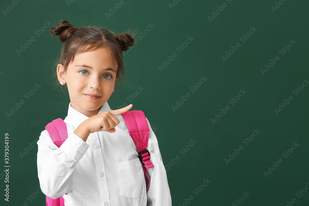 Little schoolgirl pointing at something on color background