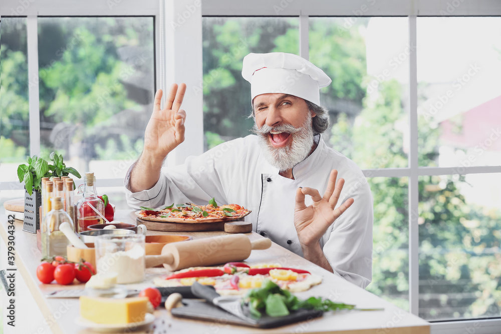 Mature male chef with tasty pizza in kitchen Mature male chef with tasty pizza in kitchen