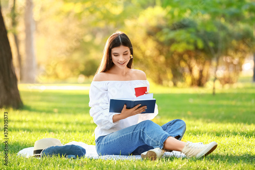 Beautiful young woman drinking coffee and reading book in park