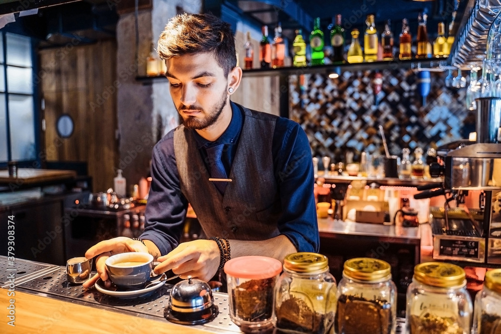 Professional bartender waiter with smile serving coffee to young woman. Regular visitor, sitting at the bar, communicating with interest with the barista. In favorite cafe with pleasant, yellow light Professional bartender waiter with smile serving coffee to young woman. Regular visitor, sitting at the bar, communicating with interest with the barista. In favorite cafe with pleasant, yellow light