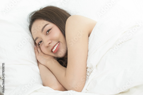 Asian women wake up happy and smile on white bed in bedroom.