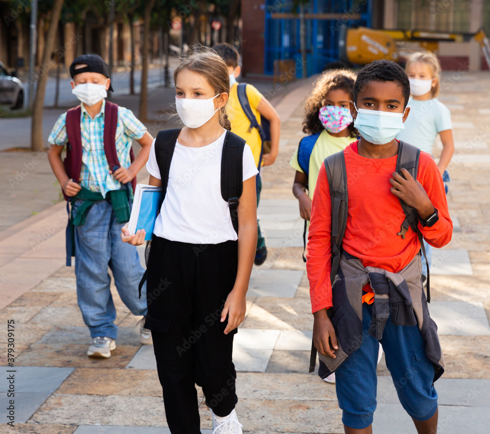 Portrait of tween boys and girls in protective masks with backpacks going to school lessons on sunny autumn day. New lifestyle during coronavirus pandemic