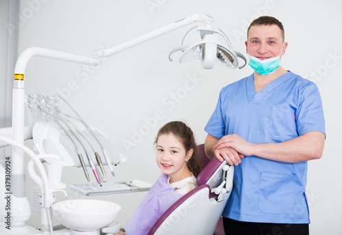 Portrait of smiling teenage girl sitting in dental chair and positive professional stomatologist in dental clinic