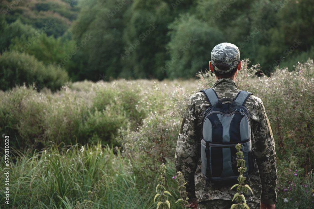 A man in a camouflage uniform with a backpack behind his back stands against the background of the forest
A man in a camouflage uniform with a backpack behind his back stands against the background of the forest