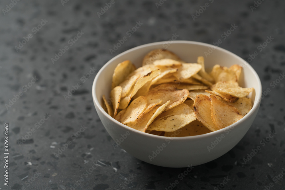 Potato chip slightly sprinkled with black pepper in white bowl on concrete background with copy space Potato chip slightly sprinkled with black pepper in white bowl on concrete background with copy space