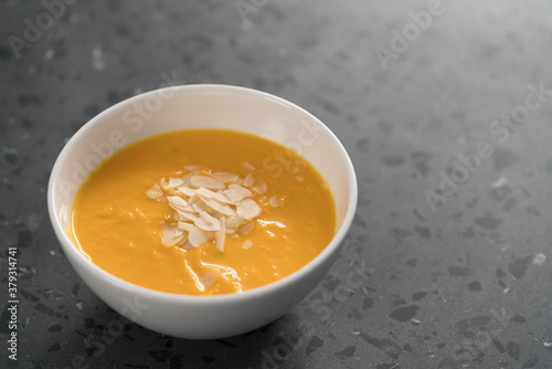 Pumpkin soup puree decorated with almond flakes in white bowl on concrete background