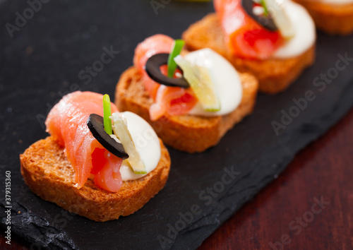 Close up image of canape with salmon and olives dressed with white sauce