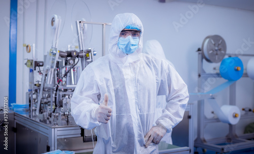 Technician worker wearing protective suite , glove are inspect machine with check face mask manufacturing process to safe and against from virus.
