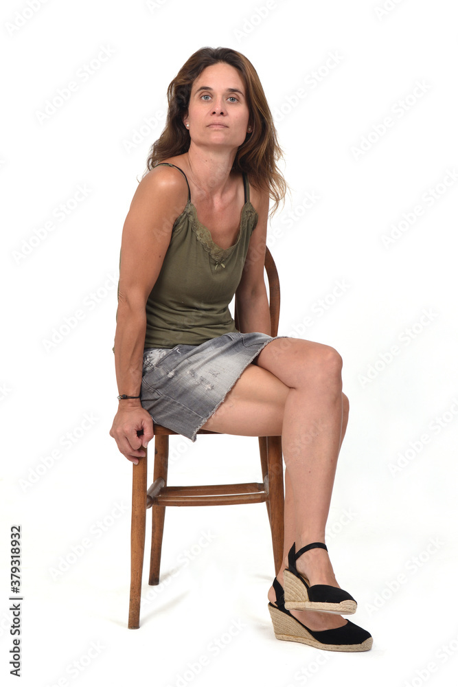 front view of a woman in denim skirt sitting on a chair and looking at camera on white background,legs crossed front view of a woman in denim skirt sitting on a chair and looking at camera on white background,legs crossed