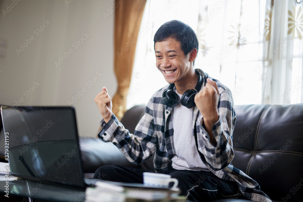 Asian student exciting in fron of laptop to hearing a good news or pass the test at home. - obrazy, fototapety, plakaty 