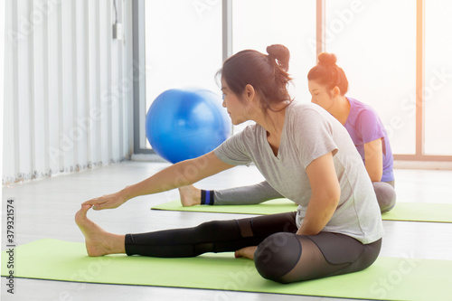 Two middle-aged Asian women doing yoga sitting on a rubber mat in a gym.