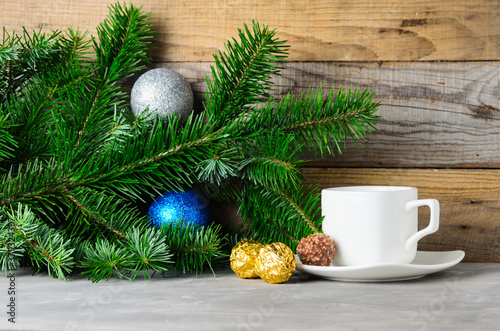 Fir branches with green needles, Christmas balls and a Cup of coffee on a saucer on a wooden background.