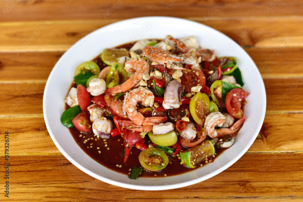 Thai Food. Green Papaya Salad (SOM-TUM) or Thai Style spicy seafood salad with shrimps, crab, Scallop, squid in a white plate on a wooden table. Thai Food. Green Papaya Salad (SOM-TUM) or Thai Style spicy seafood salad with shrimps, crab, Scallop, squid in a white plate on a wooden table.