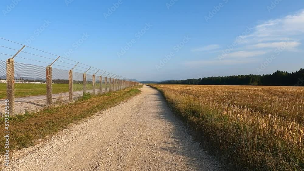 Walking on macadam unpaved gravel dirt countryside road near Ljubljana airport. Farming fields on the right side. Forward dolly moving, real time, wide angle Walking on macadam unpaved gravel dirt countryside road near Ljubljana airport. Farming fields on the right side. Forward dolly moving, real time, wide angle