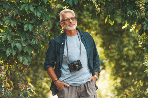 Фотография A confident elderly man walks with a camera in a city park.