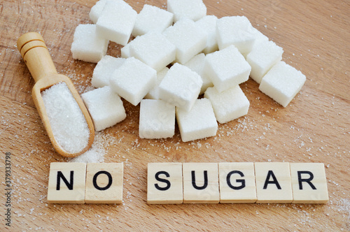 Refined sugar and wooden spoon with loose sugar on wooden background. Word no sugar of wooden blocks with letters photo