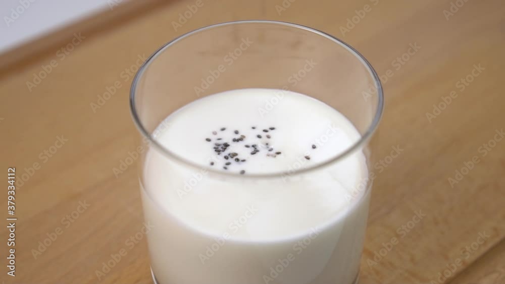 Chia seeds are poured into a glass of yogurt or thick kefir. On a wooden cutting board. Healthy breakfast and superfood. Close up. Slow motion Chia seeds are poured into a glass of yogurt or thick kefir. On a wooden cutting board. Healthy breakfast and superfood. Close up. Slow motion