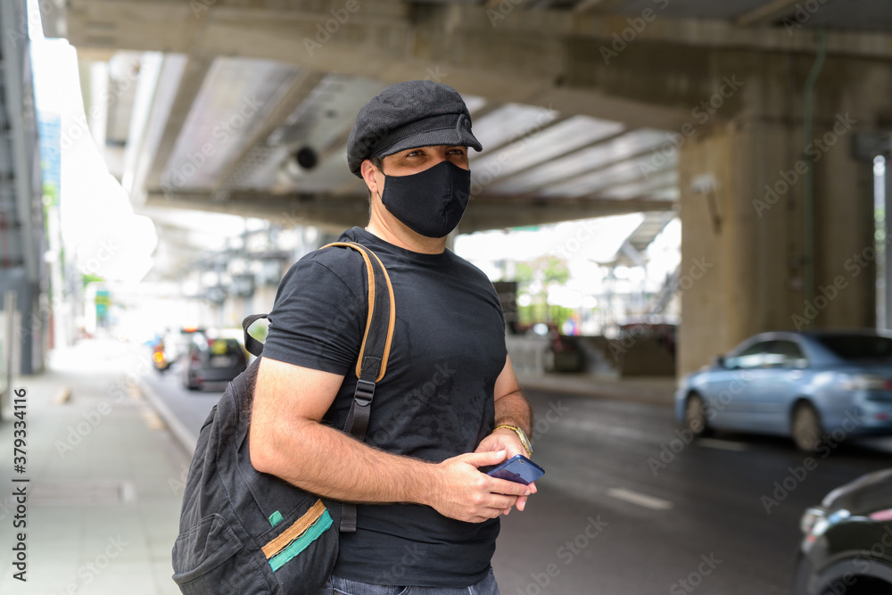 Portrait of Persian tourist man with backpack wearing mask while waiting for the taxi