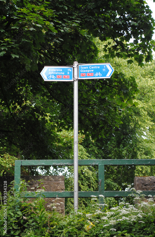Rural Sign Post with Metal Pole & Directions beside Wooden Fence & Trees 