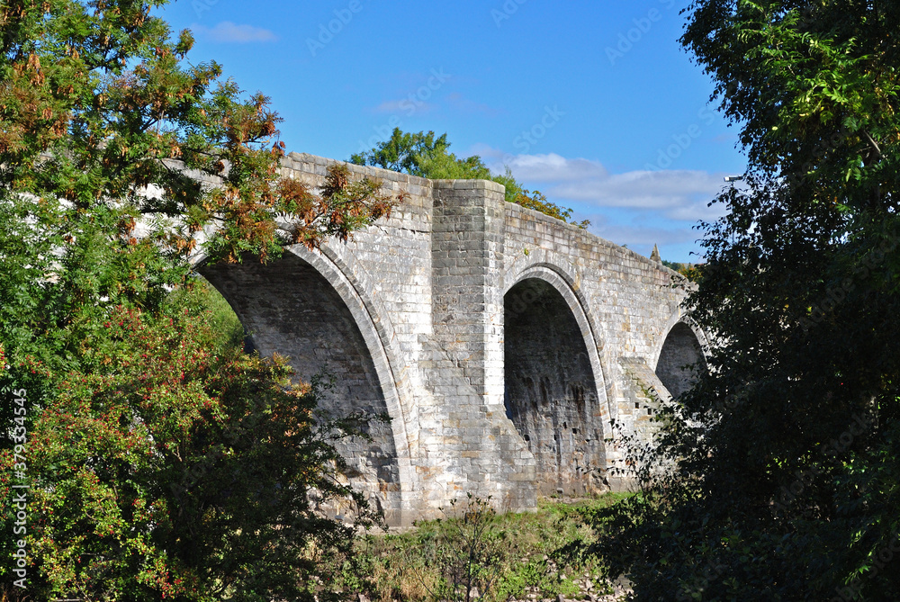 Ancient Stone River Bridge with Arches against Blue Sky 