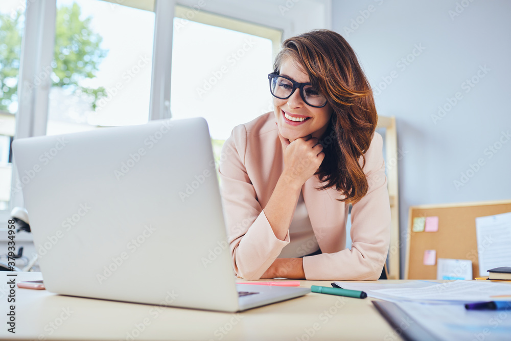Smiling woman looking on laptop while working in small office or home office Smiling woman looking on laptop while working in small office or home office